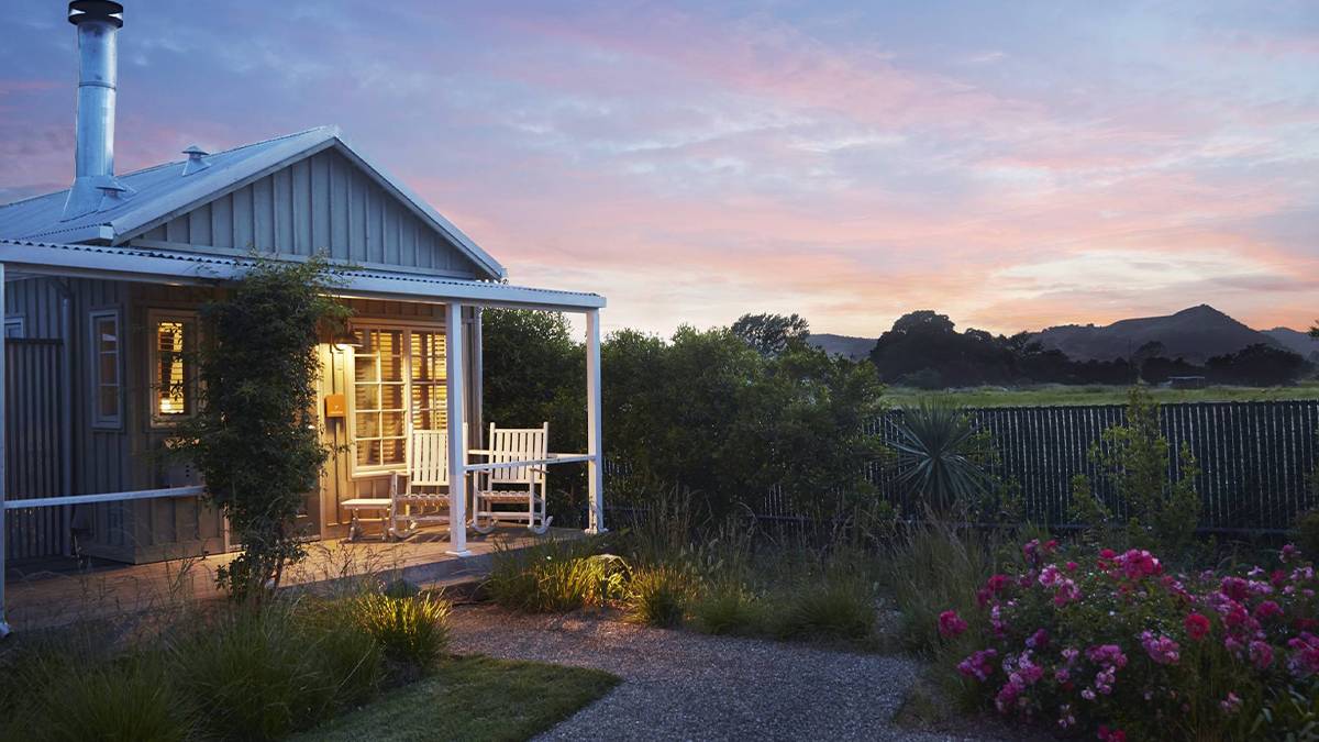 View of a couples cabin on the left with grey siding and a ranch with mountains and a sunset behind it on the right at Carneros Resort & Spa in San Francisco, California, USA